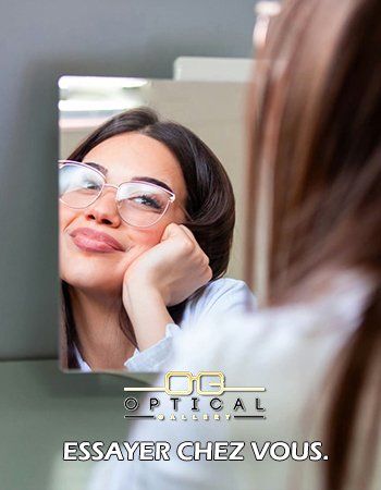 Femme souriante s'observant dans un miroir en essayant une monture de lunettes élégante - Optical Gallery.