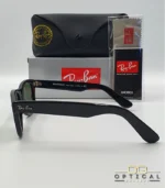 Lunettes de soleil Ray-Ban Wayfarer RB2140 noires avec verres verts G-15, présentées avec leur étui noir, leur boîte grise et leur kit de nettoyage, le tout sur fond blanc avec le logo Optical Gallery.
