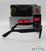 Lunettes de soleil Ray-Ban Wayfarer RB2140 noires avec verres verts G-15, présentées avec leur étui noir, leur boîte grise et leur kit de nettoyage, le tout sur fond blanc avec le logo Optical Gallery.