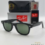 Lunettes de soleil Ray-Ban Wayfarer RB2140 noires avec verres verts G-15, présentées avec leur étui noir, leur boîte grise et leur kit de nettoyage, le tout sur fond blanc avec le logo Optical Gallery.