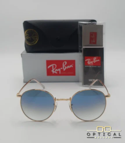 Lunettes de soleil Ray-Ban New Round RB3637 dorées avec verres dégradés bleus gris, étui noir, boîte grise et livret de garantie chez Optical Gallery.