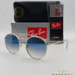 Lunettes de soleil Ray-Ban Round Double Bridge RB3647N dorées avec cerclages en acétate transparent et verres dégradés bleus, étui noir, boîte grise et livret de garantie chez Optical Gallery.