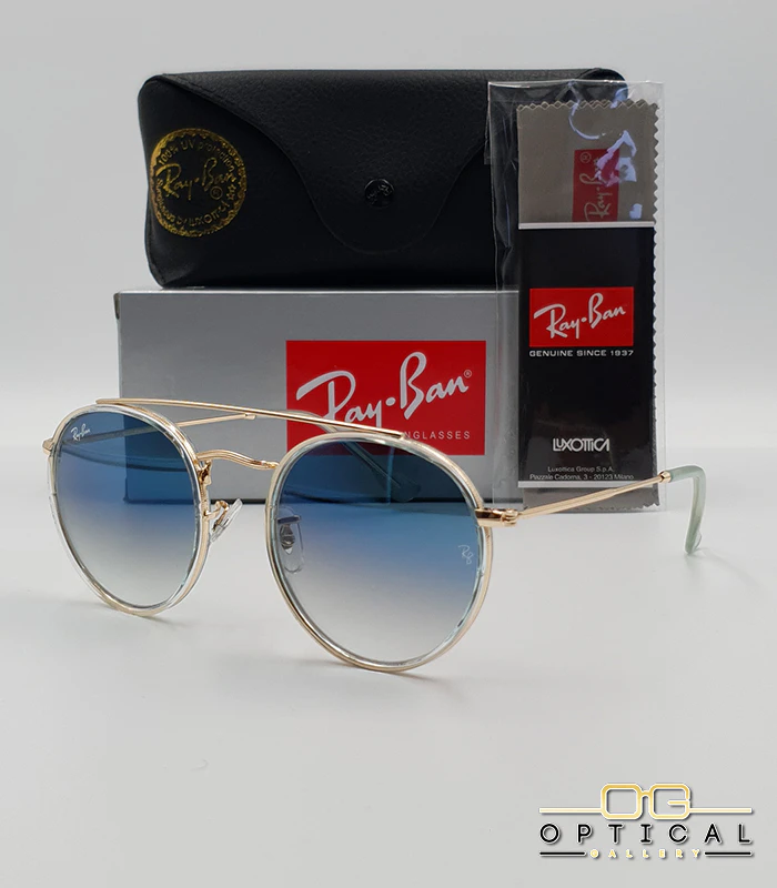 lunettes-de-soleil-ray-ban-round-double-bridge-rb3647n-or-transparent-bleu-degrade-optical-gallery Lunettes de soleil Ray-Ban Round Double Bridge RB3647N dorées avec cerclages en acétate transparent et verres dégradés bleus, étui noir, boîte grise et livret de garantie chez Optical Gallery.