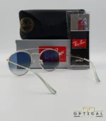 Lunettes de soleil Ray-Ban Round Double Bridge RB3647N dorées avec cerclages en acétate transparent et verres dégradés bleus, étui noir, boîte grise et livret de garantie chez Optical Gallery.