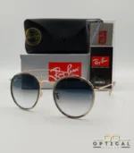Lunettes de soleil Ray-Ban Round Double Bridge RB3647N dorées avec cerclages en acétate transparent et verres dégradés bleus, étui noir, boîte grise et livret de garantie chez Optical Gallery.