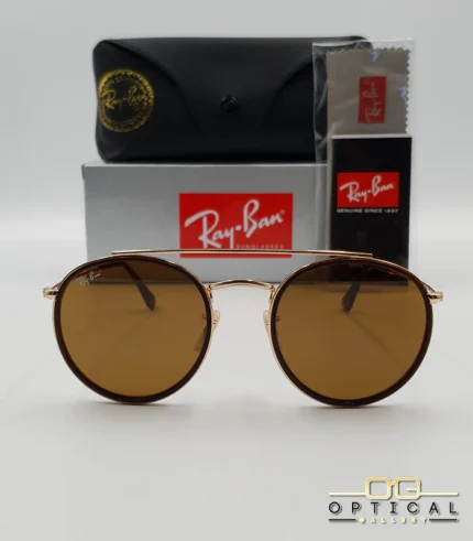 Lunettes de soleil Ray-Ban Round Double Bridge RB3647N dorées avec cerclages en acétate marron et verres marrons B-15, étui noir, boîte grise et livret de garantie chez Optical Gallery.