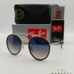 Lunettes de soleil Ray-Ban Round Double Bridge RB3647N dorées avec cerclages en acétate bleu marine et verres dégradés bleus marrons, étui noir, boîte grise et livret de garantie chez Optical Gallery.