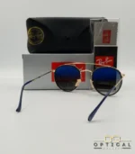 Lunettes de soleil Ray-Ban Round Double Bridge RB3647N dorées avec cerclages en acétate bleu marine et verres dégradés bleus marrons, étui noir, boîte grise et livret de garantie chez Optical Gallery.