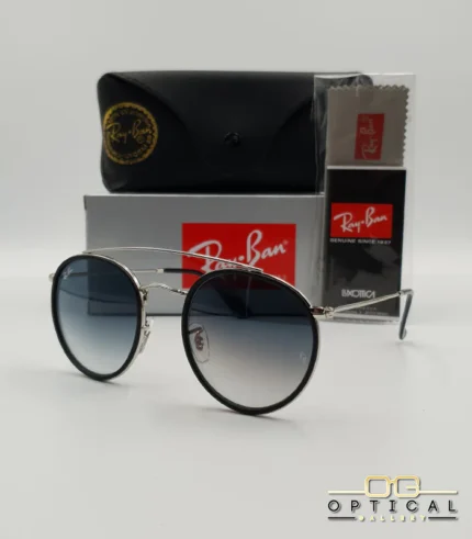 Lunettes de soleil Ray-Ban Round Double Bridge RB3647N argentées avec cerclages en acétate noir et verres dégradés bleus gris, étui noir, boîte grise et livret de garantie chez Optical Gallery.