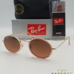 Lunettes de soleil Ray-Ban Round Double Bridge RB3847N dorées avec cerclages en acétate rose transparent et verres dégradés marrons, étui noir, boîte grise et livret de garantie chez Optical Gallery.
