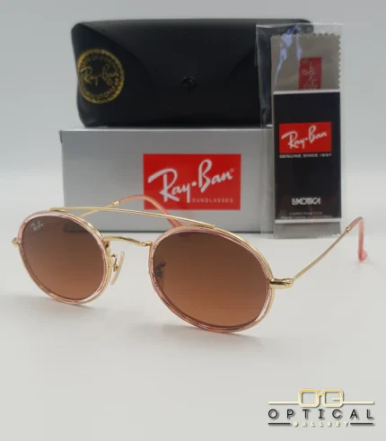 Lunettes de soleil Ray-Ban Round Double Bridge RB3847N dorées avec cerclages en acétate rose transparent et verres dégradés marrons, étui noir, boîte grise et livret de garantie chez Optical Gallery.
