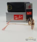 Lunettes de soleil Ray-Ban Round Double Bridge RB3847N dorées avec cerclages en acétate rose transparent et verres dégradés marrons, étui noir, boîte grise et livret de garantie chez Optical Gallery.