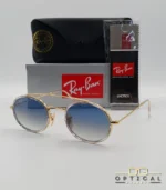 Lunettes de soleil Ray-Ban Round Double Bridge RB3847N dorées avec cerclages en acétate transparent et verres dégradés bleus gris, étui noir, boîte grise et livret de garantie chez Optical Gallery.