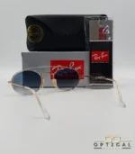 Lunettes de soleil Ray-Ban Round Double Bridge RB3847N dorées avec cerclages en acétate transparent et verres dégradés bleus gris, étui noir, boîte grise et livret de garantie chez Optical Gallery.