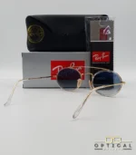 Lunettes de soleil Ray-Ban Round Double Bridge RB3847N dorées avec cerclages en acétate transparent et verres dégradés bleus gris, étui noir, boîte grise et livret de garantie chez Optical Gallery.