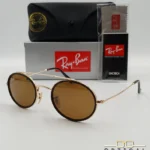 Lunettes de soleil Ray-Ban Round Double Bridge RB3847N dorées avec cerclages en acétate noir et verres marrons B-15, étui noir, boîte grise et livret de garantie chez Optical Gallery.