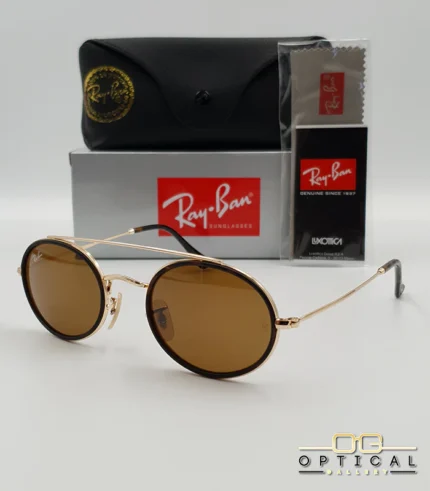 Lunettes de soleil Ray-Ban Round Double Bridge RB3847N dorées avec cerclages en acétate noir et verres marrons B-15, étui noir, boîte grise et livret de garantie chez Optical Gallery.