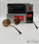 Lunettes de soleil Ray-Ban Round Double Bridge RB3847N dorées avec cerclages en acétate noir et verres marrons B-15, étui noir, boîte grise et livret de garantie chez Optical Gallery.