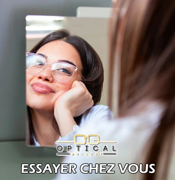 Jeune femme souriante se regardant dans un miroir en essayant des lunettes de vue dorées élégantes avec le logo Optical Gallery et l'inscription Essayer Chez Vous.
